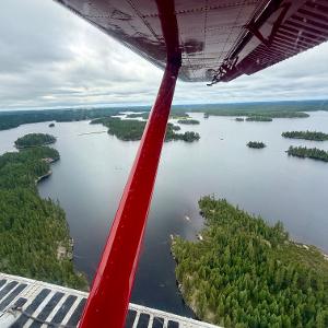 View from a red floatplane window showing a vast lake with many forested islands under a cloudy sky in the Canadian wilderness.
