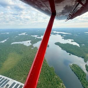 View from a red Beaver plane flying over a vast network of lakes and evergreen forests in the Canadian North.