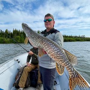 An angler in a boat holds up a massive Northern Pike caught on a remote Canadian lake.